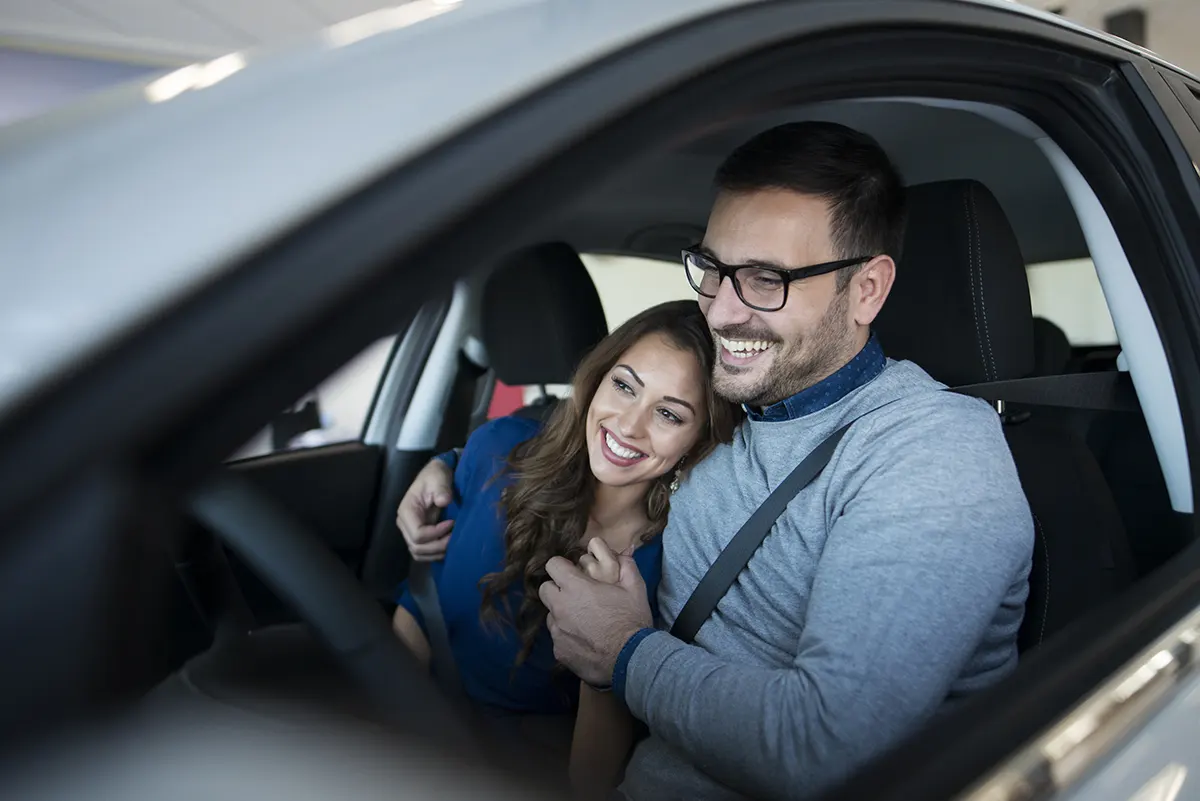 oareja joven de hombre y mujer sonriendo abrazados dentro de un auto