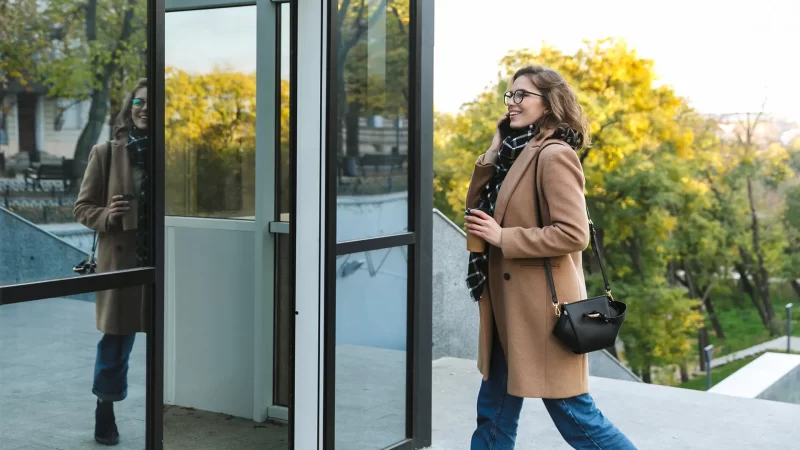 joven mujer sonriendo con un café en la mano entrando a un edificio