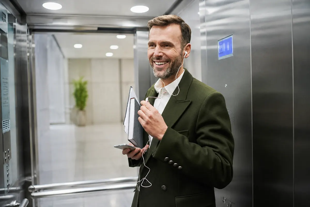 hombre sonriendo en un elevador hablando por teléfono con auriculares