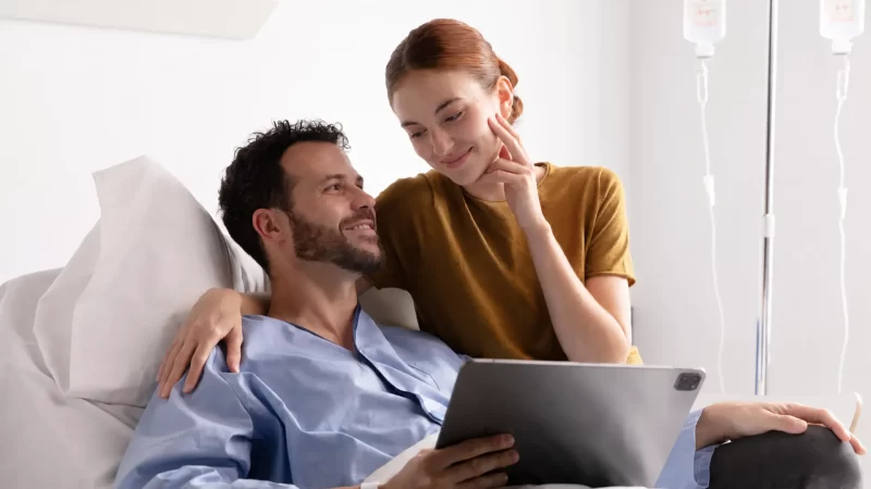 pareja feliz sonriendo en cama de hospital mientras miran una tablet