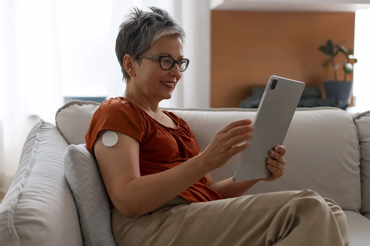 mujer madura con diabetes sentada en sillón leyendo en una tablet