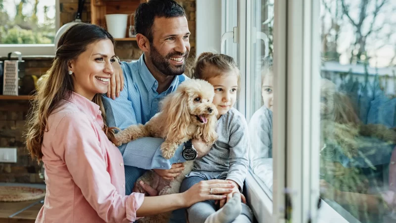 familia feliz sonriendo frente a la ventana con su perrito