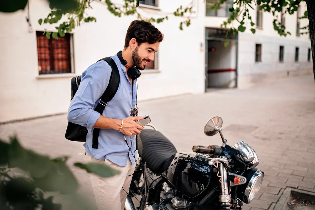 hombre joven sonriendo mientras junto a su moto en el exterior