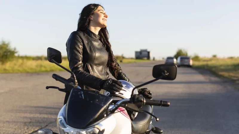 mujer sonriendo junto a su moto a la luz del sol en el exterior