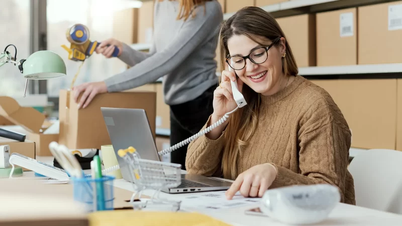 mujer sonriendo hablando por teléfono en su escritorio mientras revisa una ficha