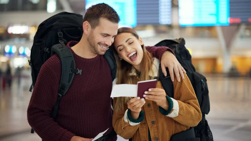 pareja feliz sonriendo en un aeropuerto mientras mira su pasaje de avión